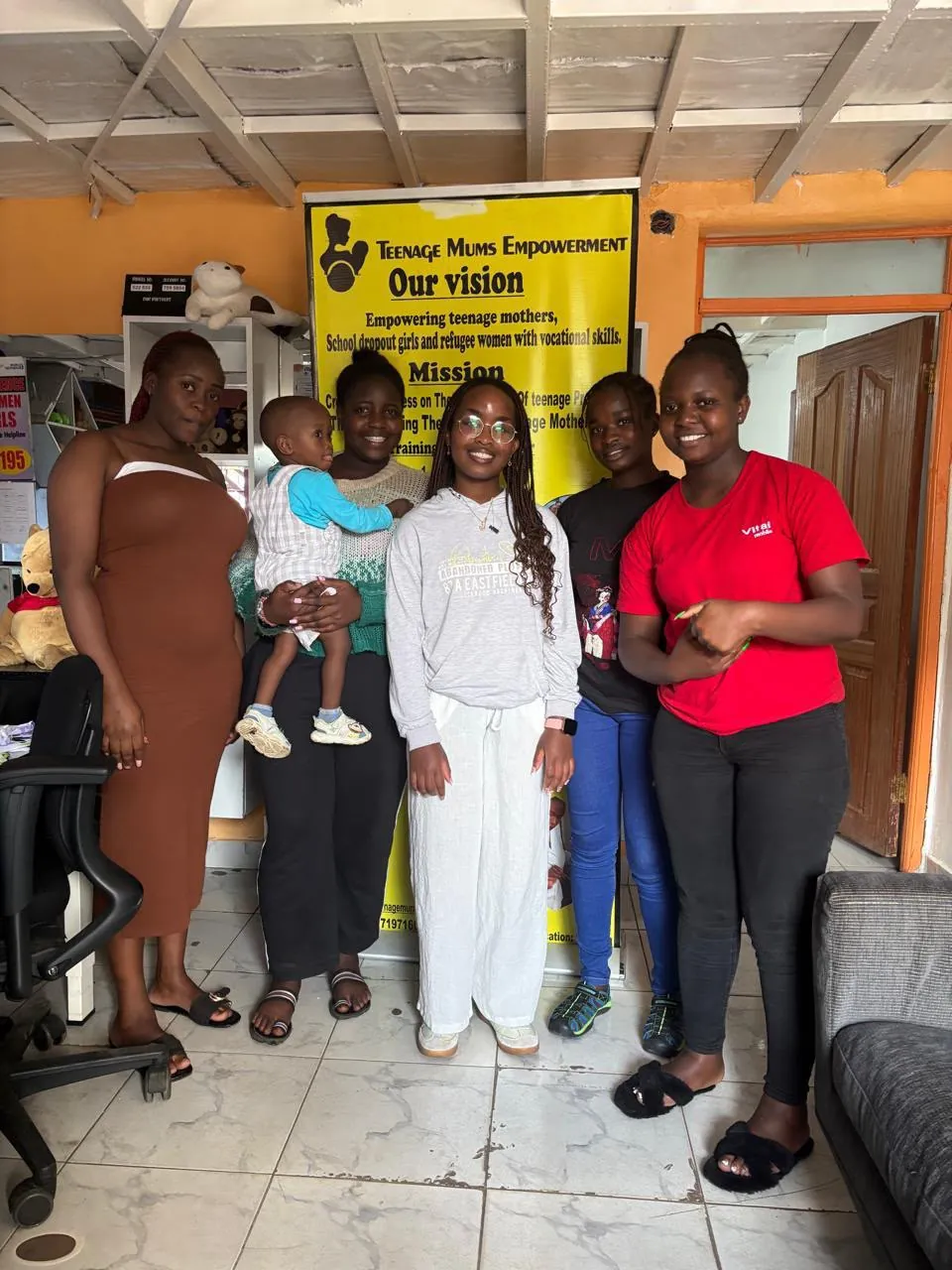 Team members and a baby standing in front of the vision and mission banner