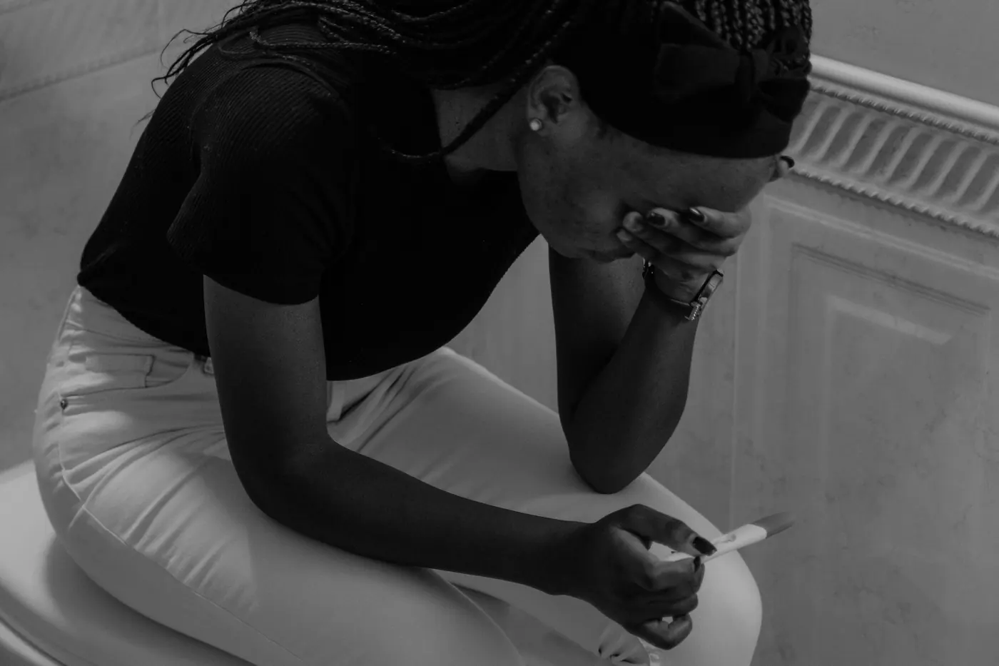 A young woman sitting with her head in her hand, holding a pregnancy test